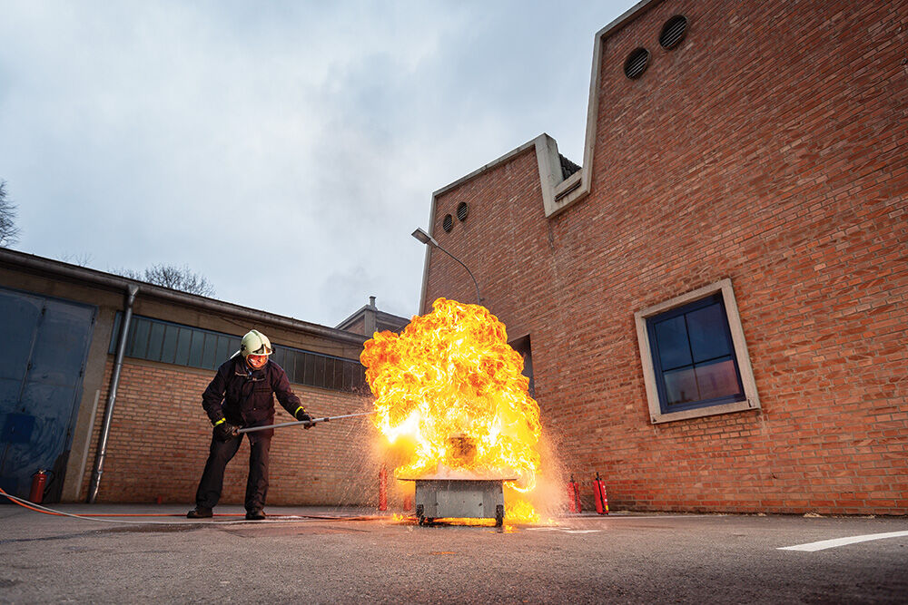 Mann mit Helm, der ein Feuer in einem Kurs löscht